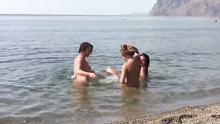 Three naked beauties on the crest of a wave at the public beach