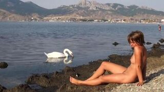 A girl is completely naked on the riverbank and enjoys herself