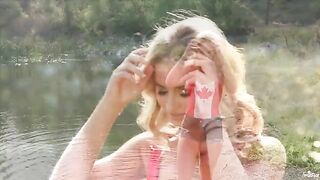 A blonde girl caresses herself tenderly on the lake’s shore
